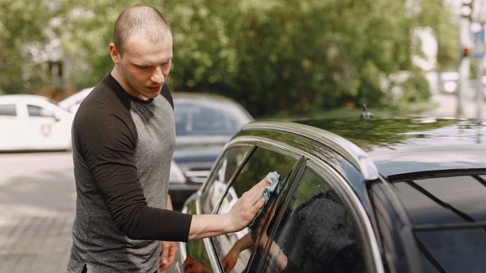 Mann wischt mit einem Tuch die Seitenscheibe eines geparkten Autos